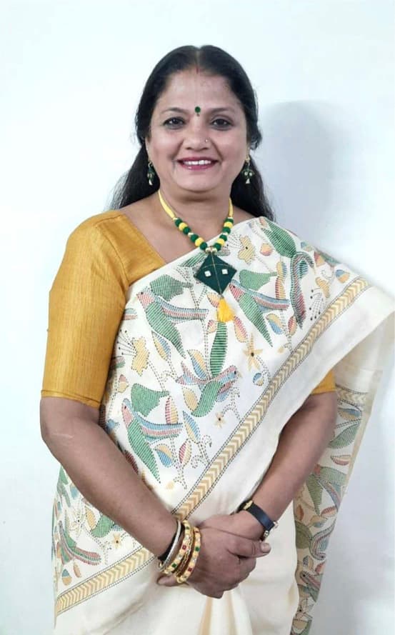 Bhavna Mehta, smiling in a marigold blouse and folk-art sari, wearing a kite-shaped pendant